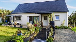 A single-story house with a dark blue roof, a covered patio area, and a garden with various plants. - Nice home in Saint-Yvi with WiFi (Saint-Yvi)