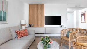 Ett modernt vardagsrum med en soffa, ett soffbord, flätade stolar, en platt-TV och en väggpanel i trä.