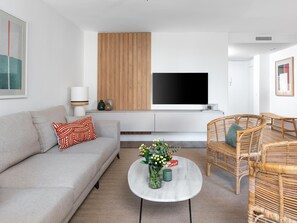 A modern living room with a sofa, coffee table, wicker chairs, a flat-screen TV, and a wooden panel wall. - Central Malaga Apartment with Private Parking (Málaga)