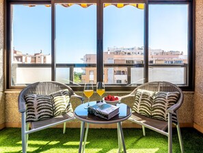A balcony with two wicker chairs, a small round table with a book, glasses, and a bowl of strawberries. - Central Malaga Apartment with Private Parking (Málaga)