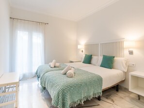 A hotel room with two beds, a small table, a nightstand, and a window with curtains. - Spacious apartment near La Malagueta Beach, Málaga (Málaga)