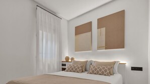 Un dormitorio moderno con una cama grande, una mesita de noche con objetos decorativos y dos espejos montados en la pared.