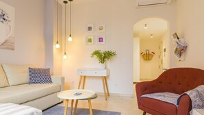 A modern living room with a sofa, a red armchair, a small round table, and a white cabinet. There are three pendant lights hanging from the ceiling, and a potted plant on the cabinet. - Charming Apt in the heart of Malaga with rooftop pool (Málaga)