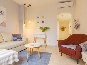 A modern living room with a sofa, a red armchair, a small round table, and a white cabinet. There are three pendant lights hanging from the ceiling, and a potted plant on the cabinet. - Charming Apt in the heart of Malaga with rooftop pool (Málaga)
