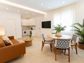 A modern living room with a sofa, a round dining table with chairs, a small coffee table, and a kitchen in the background. - Bright apartment, shared pool, beach access (Chilches)