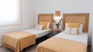 Habitació d'hotel amb dos llits individuals, cadascun amb un capçal de fusta i una taula de nit.