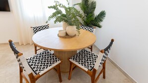 Taula rodona de fusta per dinar amb dues cadires, cadascuna amb coixí estampat en blanc i negre. Hi ha dues plantes en testos a la taula, una amb fulles amples i l'altra amb fulles llargues i allargassades.