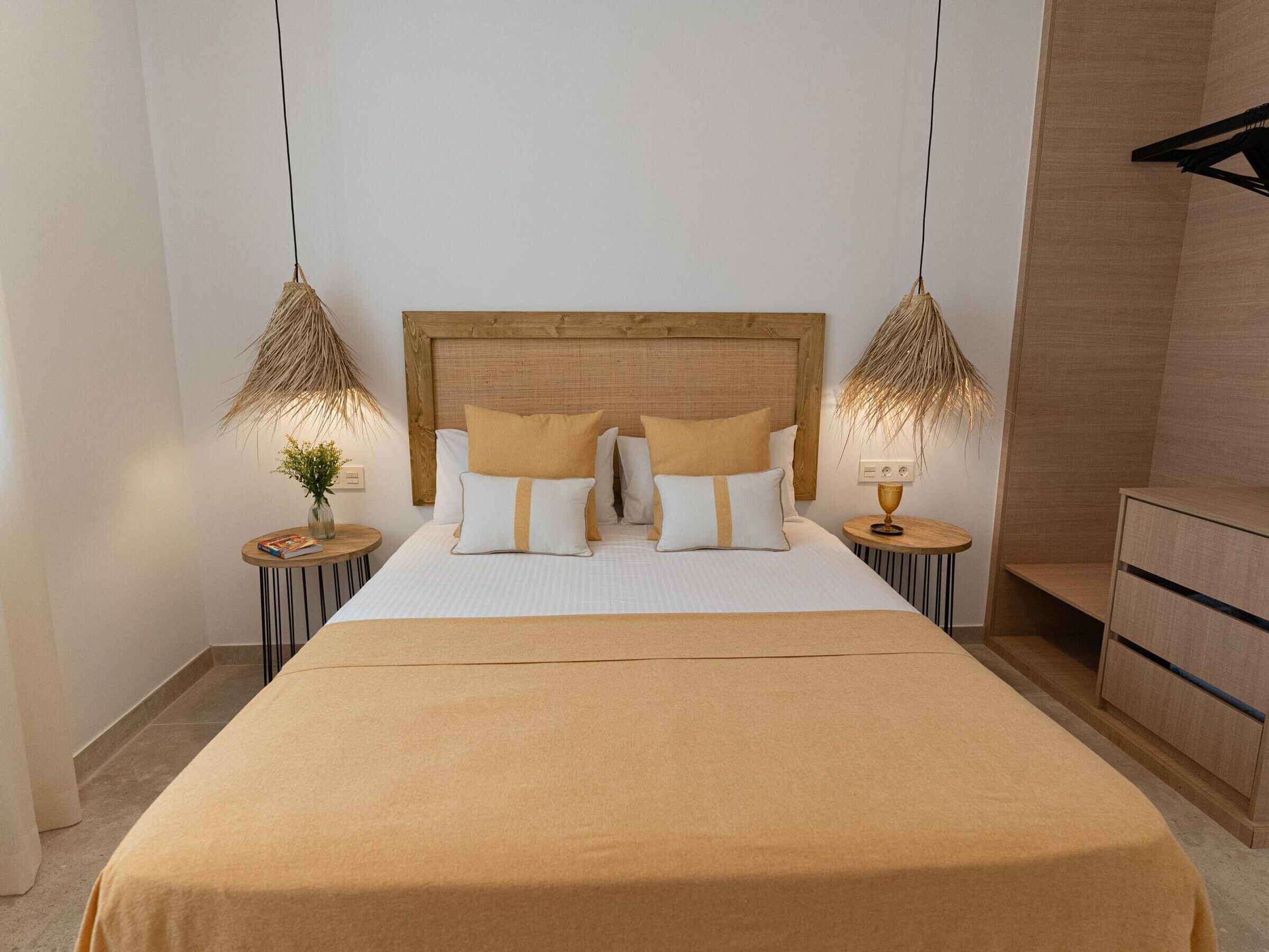 Habitación de hotel con una cama grande, cabecera de madera, dos mesitas de noche con lámparas y un armario de madera.