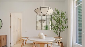 Un comedor con una mesa redonda, cuatro sillas, una lámpara colgante, una planta en maceta y una puerta.