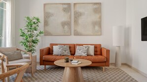 Una sala de estar moderna con un sofá de cuero, dos obras de arte abstractas en la pared, una mesa de centro de madera, una planta en maceta y una lámpara.