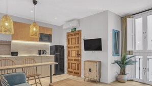 Een moderne keuken met houten kastjes, een zwarte koelkast en een magnetron. Er is een eethoek met een houten tafel en stoelen, en een groot raam met gordijnen.