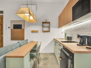 A compact kitchen with a wooden countertop, a built-in oven, and a microwave. There is a bench with chairs, a small shelf, and a hanging light fixture. - Modern Studio at the Heart of Málaga's Historic Center (Málaga)