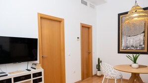 Un soggiorno moderno con una televisione a schermo piatto, porte in legno, un tavolo da pranzo rotondo con una sedia bianca, una pianta in vaso e un quadro astratto incorniciato.