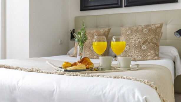 Una cama bien hecha con una bandeja de croissants, jugo de naranja y una taza de café.