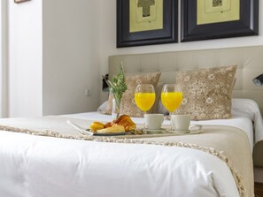 Una cama bien hecha con una bandeja de croissants, jugo de naranja y una taza de café.