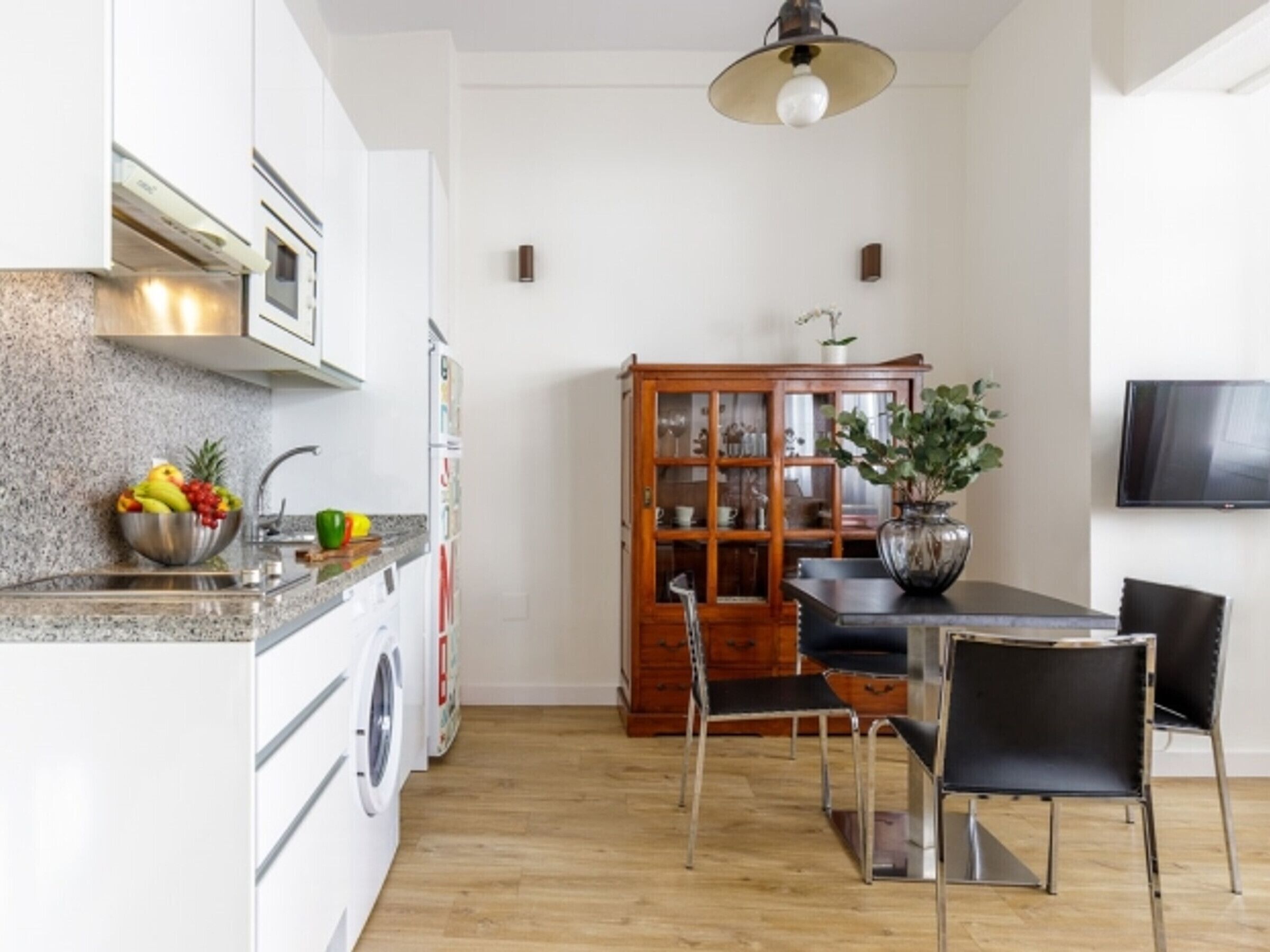 A modern kitchen with granite countertops, a built-in washing machine, a dining table with chairs, and a large wooden cabinet.