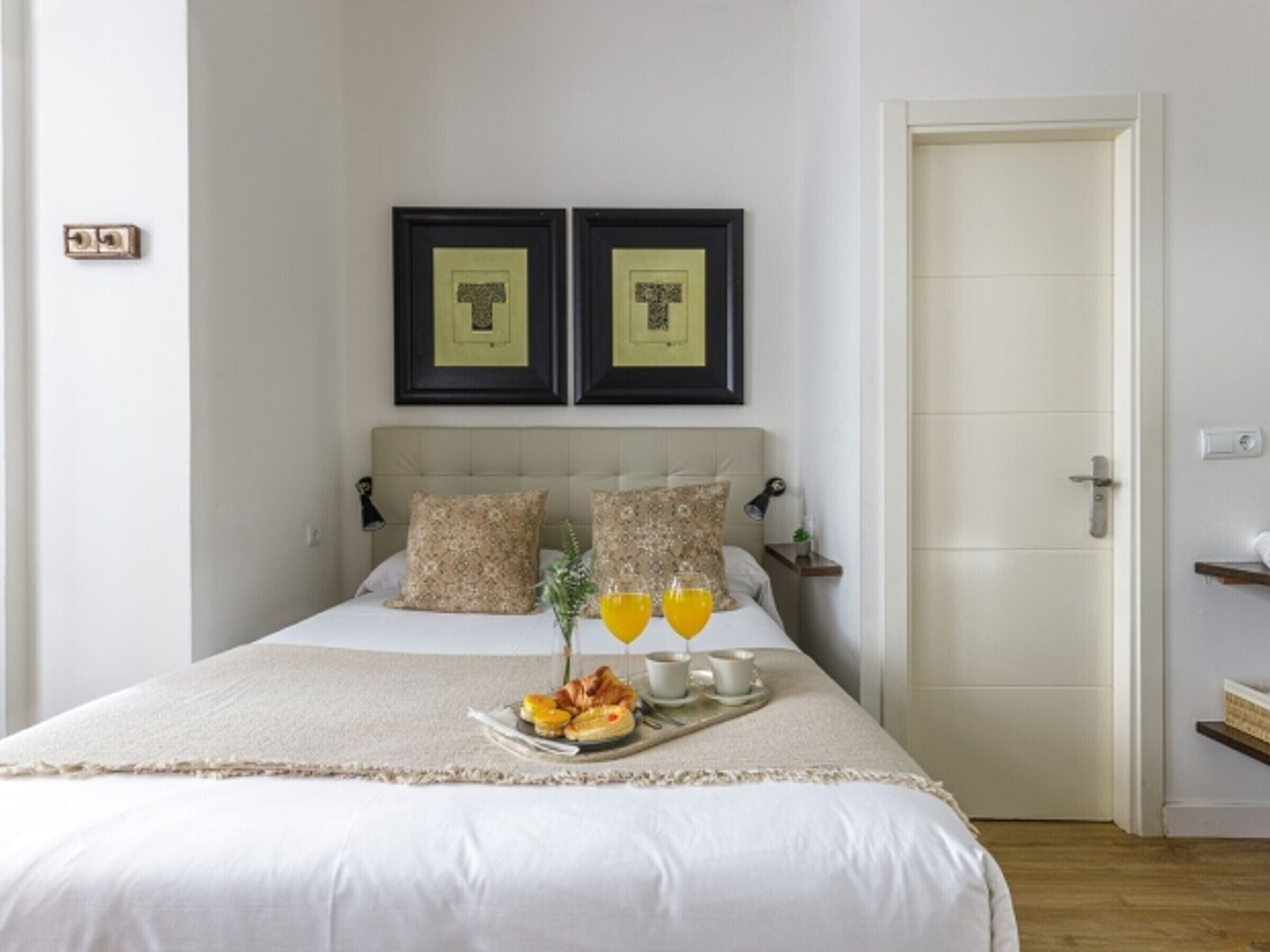 A neatly made bed with a tray of breakfast items and two framed pictures above it.