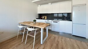 A modern kitchen with white cabinets, a wooden dining table with two chairs, and a built-in oven. - Elegant Accommodation in Malaga - Ideal for Groups (Málaga)