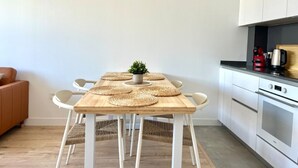 A modern kitchen with white cabinets, a wooden dining table with woven placemats, and a small potted plant. - Elegant Accommodation in Malaga - Ideal for Groups (Málaga)