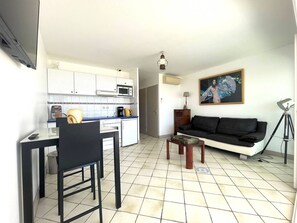 A compact living space with a kitchenette, a dining area, a sofa, and a painting on the wall. - Premium Apartment 2P South Cap d'Agde (Cap d'Agde)