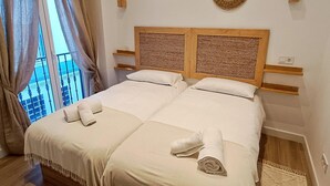 A double bed with two pillows, a wooden headboard, and a window with curtains. - Charming apartment in Malaga (Málaga)