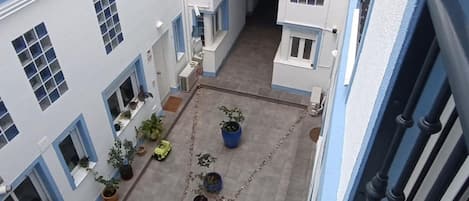 A courtyard with potted plants, a yellow toy car, and a chain-link fence.