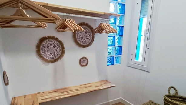 A room with a wooden bench, wall-mounted shelves, and a hanging rack with wooden hangers. - Charming apartment in Malaga (Málaga)