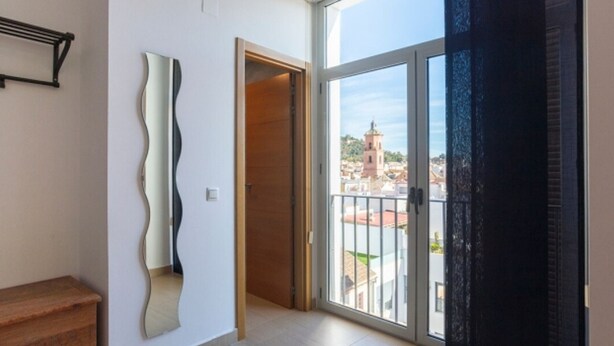 Una habitació àmplia amb un gran finestral corredís que dona a un balcó amb vista a la ciutat.