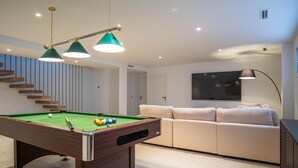Ein modernes Wohnzimmer mit Billardtisch, einer Couch und einem Fernseher.