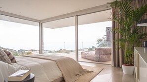 Ein modernes Schlafzimmer mit einem großen Bett, Blick auf die Stadt und einem Balkon mit einem Sessel.