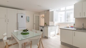 Ett modernt kök med vita skåp, ett matbord i glas och en inbyggd tvättmaskin.