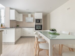 A modern kitchen with white cabinets, a microwave, oven, and a glass dining table with chairs. - Stunning duplex in Malaga center with private terrace (Málaga)