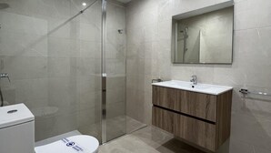 Un baño moderno con ducha de vidrio, inodoro y tocador con espejo.