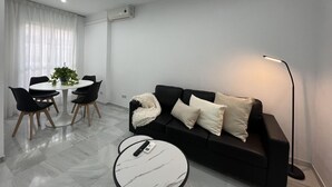 Una sala moderna con un sofá negro, una mesa redonda de centro, una mesa de comedor con sillas y una planta en maceta.