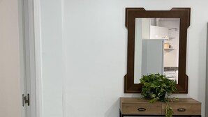 Un baño con pared blanca, tocador de madera con espejo y planta en maceta.