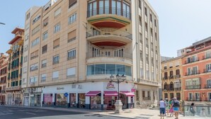 Un hôtel à plusieurs étages, doté d’une façade incurvée sur un coin, de grandes fenêtres et d’un magasin situé au rez-de-chaussée.