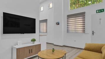 Un área de espera moderna con una televisión de pantalla plana, un mueble de madera, una mesa redonda con una planta y un sofá amarillo.