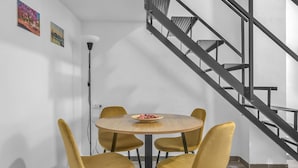 Uma sala de jantar com uma mesa redonda e quatro cadeiras amarelas, uma escada com grades de metal e dois quadros pendurados na parede.