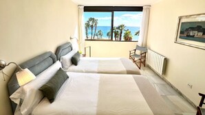 Ett hotellrum med två sängar, utsikt över stranden och en takfläkt.