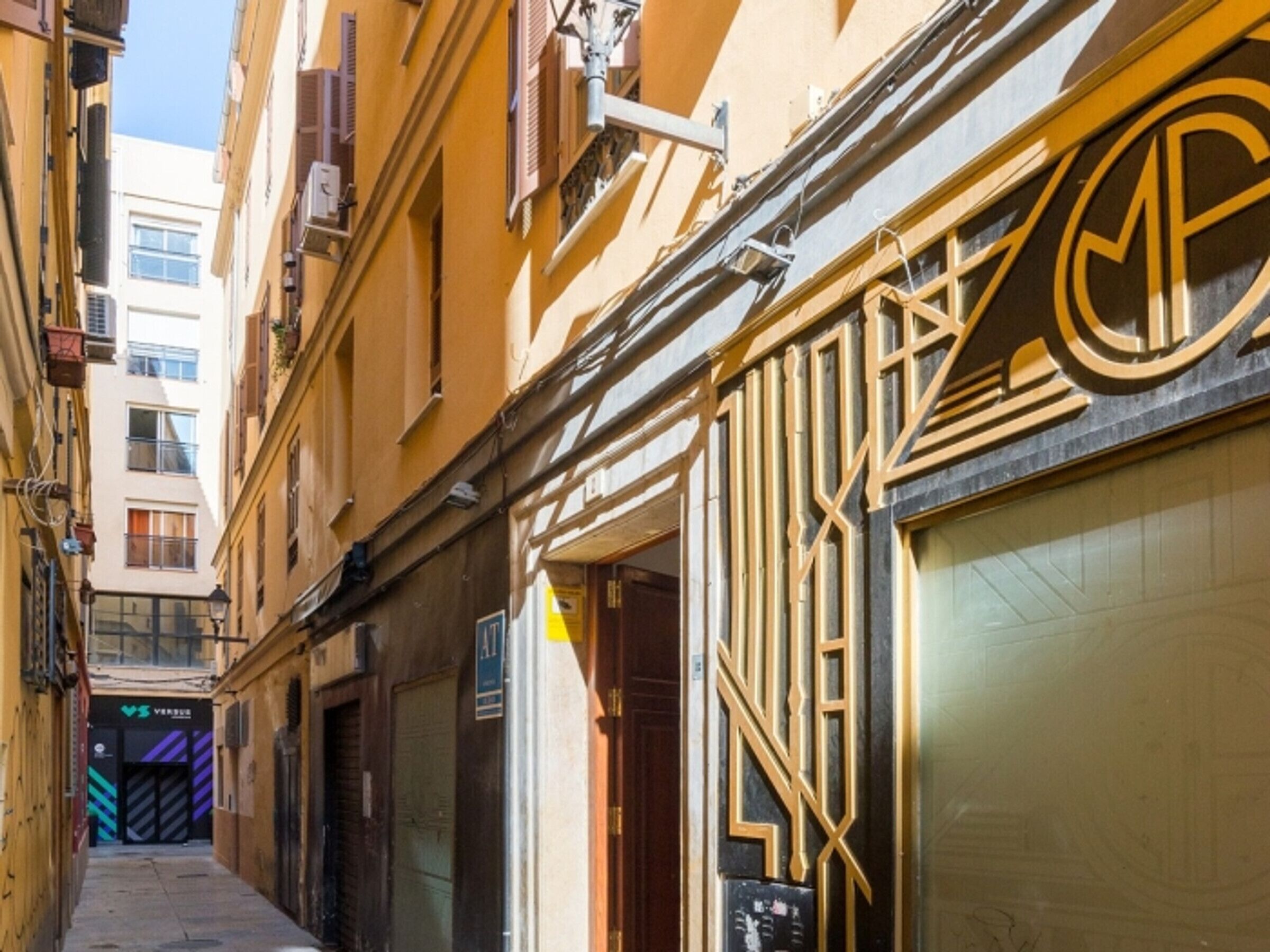 Une ruelle étroite entre deux bâtiments, avec un magasin fermé dont la façade présente un motif géométrique.