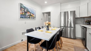 Une cuisine moderne avec des meubles blancs, un réfrigérateur en acier inoxydable et un coin repas avec une table blanche dressée pour quatre personnes.