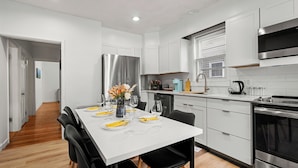 Une cuisine moderne avec des meubles blancs, des appareils en acier inoxydable et un coin repas doté d’une table blanche, mise pour quatre personnes.