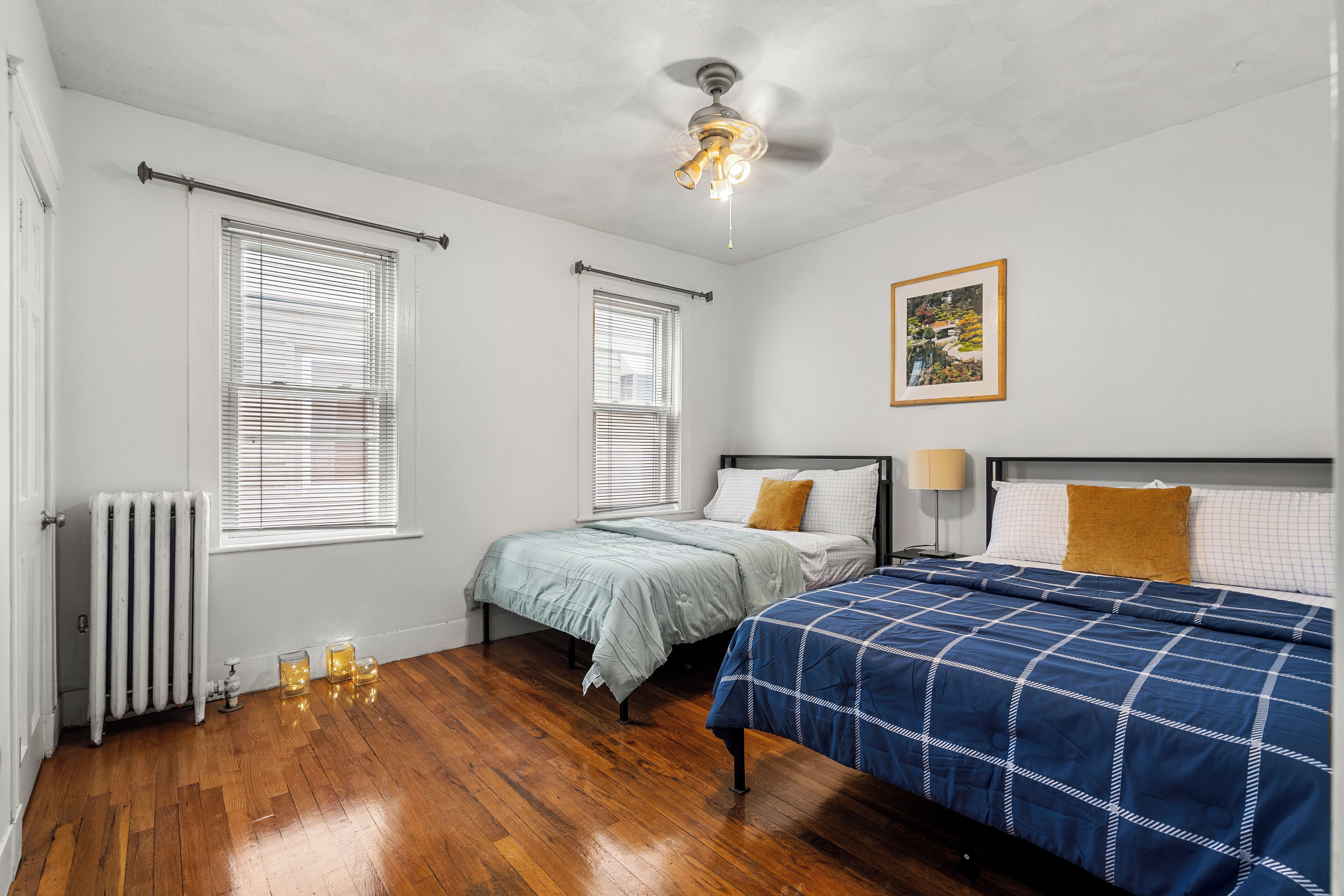 A bedroom with two beds, a ceiling fan, and a radiator.