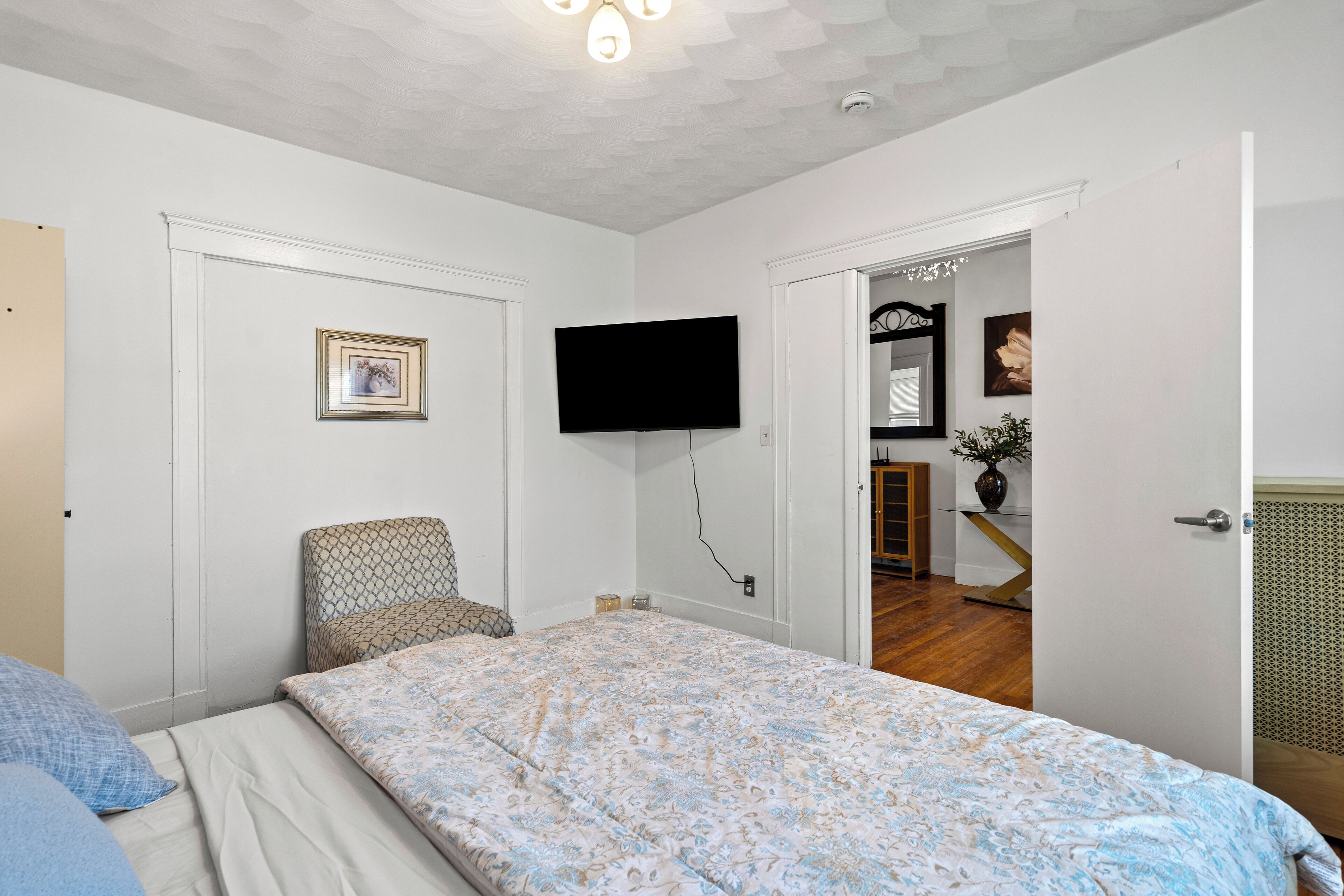 A bedroom with a bed, a chair, a television, and a door leading to another room.