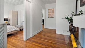 Une chambre moderne avec un plancher en bois, un lit recouvert d’une couvre-lit à motifs, une armoire et une table de chevet avec une lampe.