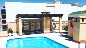 Ein Swimmingpool mit Sonnensegel, Liegestühlen und einer roten Rutsche.