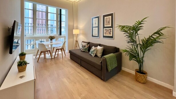 Una sala de estar moderna con un sofá, una mesa de comedor con sillas, un televisor y cuadros en la pared.