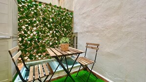 Un pequeño espacio al aire libre con mesa y sillas de madera, una mesa con superficie de vidrio y suelo de césped artificial verde.
