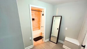 A narrow hallway with a wooden door leading to a bathroom with a bathtub and a shower. - Comfortable Westerville Apt by State Street - Great for Mid-Term, Prime Location (Westerville)