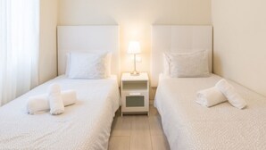 A hotel room with two single beds, each with a pillow and a rolled towel. There is a nightstand with a lamp between the beds. - Bright 3-bedroom apartment in the heart of Málaga (Málaga)